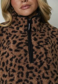 Pullover in pile marrone con stampa leopardata nera, colletto alto, chiusura con mezza zip e bordo nero, dotato di un'etichetta con logo sulla zip.