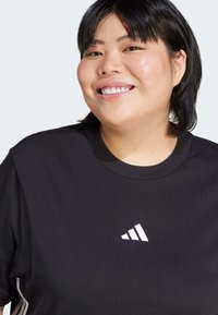 Melna īsām piedurknēm T-krekls, kas izgatavots no kokvilnas, ar apaļu kakla izgriezumu un baltu Adidas logotipu uz krūtīm. Gluda tekstūra, ikdienas dizains.