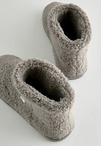 Graue, flauschige Hausschuhe mit einer weichen Textur, abgerundeter Form und niedrigem Schnitt. Gummisohlen und eine offene Spitze für einfaches Hineinschlüpfen.