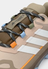 Μπεζ παπούτσι πεζοπορίας με επάνω μέρος από δίχτυ, γκρι κορδόνια, τρεις λευκές ρίγες και χρωματιστές λεπτομέρειες. Διαθέτει επένδυση στο κολάρο και υφή στη σόλα.