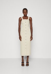 Šviesiai smėlinė midi suknelė su reguliuojamomis petnešomis, mygtukų priekine uždarymo sistema ir šoniniais kišenėmis. Pagaminta iš medvilnės audinio su lygiu paviršiumi.