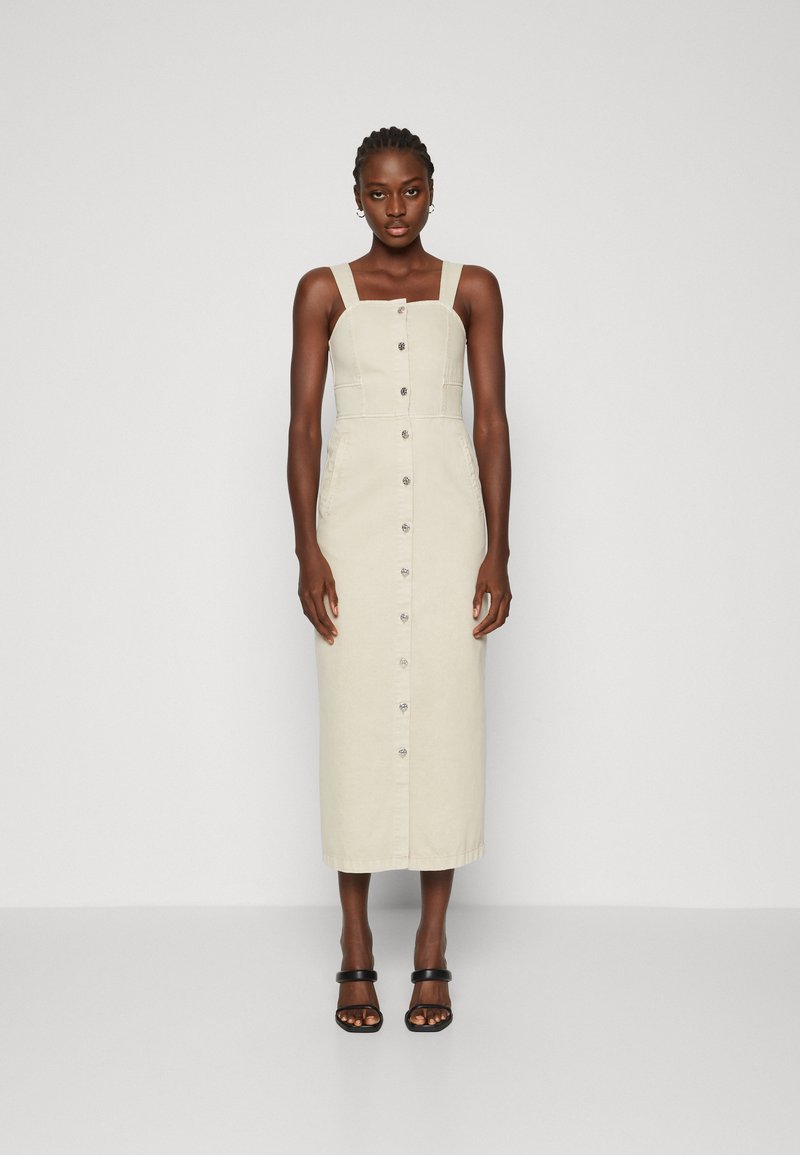 Šviesiai smėlinė midi suknelė su reguliuojamomis petnešomis, mygtukų priekine uždarymo sistema ir šoniniais kišenėmis. Pagaminta iš medvilnės audinio su lygiu paviršiumi.