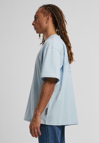 Camiseta de manga corta de color azul claro mostrada en vista lateral. Hecha de algodón suave, con un ajuste holgado y una pequeña etiqueta de la marca en el dobladillo.