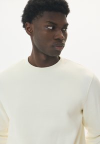 Crème sweatshirt met een ronde hals en lange mouwen. Gemaakt van zachte, gestructureerde stof. Eenvoudig ontwerp zonder zichtbare patronen of accenten.