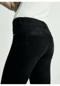 Vaqueros de mezclilla negra con diseño ajustado, cintura de altura media y dos bolsillos traseros. La tela presenta una textura suave y ligeramente desgastada.