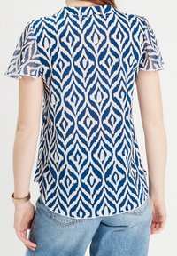 Blue and white patterned blouse with short sleeves, featuring a diamond design. Fabric appears lightweight with a slight sheen.