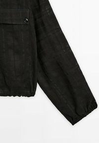 Zwarte lange mouwen top van gestructureerde stof, met een geplooide manchette en een patch pocket met een cirkelvormige knoopdetail.