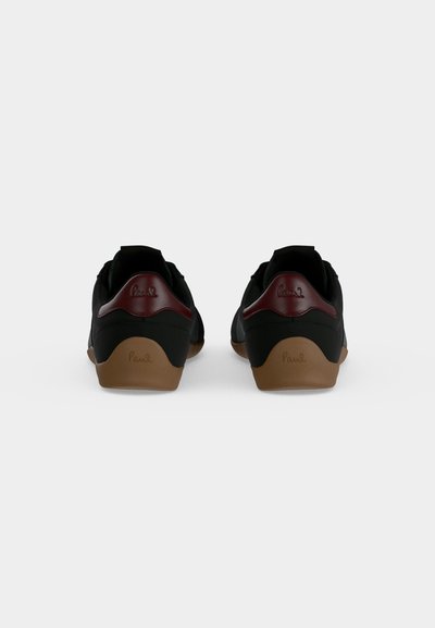 Paire de baskets basses noires avec semelles marron et accents rouge foncé au talon, vues de dos sur fond blanc.