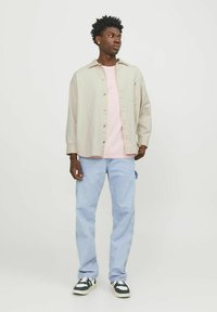 Light beige oversized shirt, pink t-shirt underneath, light blue jeans, and black and white sneakers, worn by a person standing against a white background.