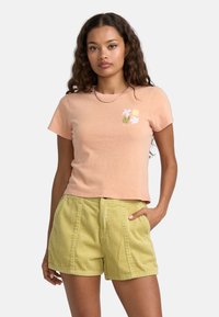 Lys rosa cropped t-shirt med blomsterdesign, parret med gule fløjlshorts med frontlommer og lodret ribbet tekstur.