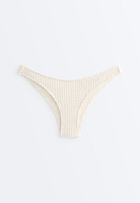 Bas de bikini taille basse en tissu crème texturé avec un motif gaufré subtil, présenté à plat sur un fond clair.