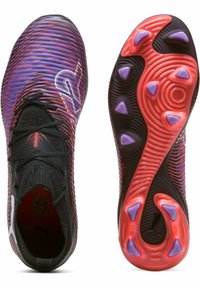 Chaussures de football avec un design rayé noir et violet, présentant un dessus texturé et une semelle rouge et noire avec des accents violets.