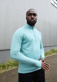 Jasnoniebieska rozpinana bluza sportowa z długim rukawem i teksturowanym materiałem. Posiada stójkę oraz subtelne logo Nike na klatce piersiowej.