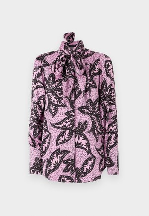 Vaaleanpunainen paita, jossa on musta kukkakuosi ja täplikkäitä yksityiskohtia, korkea kaulus ja suuri rusetti kauluksessa. Pitkät hihat.