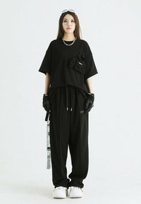 Camiseta negra de corte oversized con un detalle de bolsillo frontal, combinada con pantalones negros sueltos. Los accesorios incluyen guantes y zapatillas blancas.