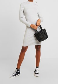 Grå långärmad klänning, knälång, gjord av ett mjukt tyg. Svart pärlhandväska med korta handtag. Svarta högstövlar.