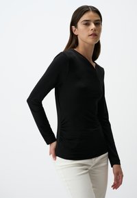 Zwart longsleeve top met V-hals, met een aansluitende pasvorm en geplooide zijdetails. Gepaard met lichte broek.