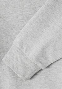 Tissu de sweat-shirt gris clair avec une manche à côtes, présentant une texture douce et un léger motif chiné, vu sous un angle.