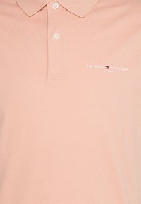 Polo i blødt lyserødt stof med en to-knaps krave, med en lille hvid broderet logo, der siger "TOMMY HILFIGER EST. 1985."
