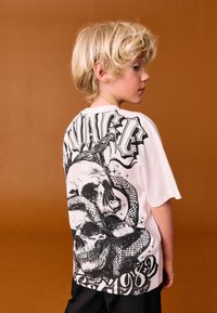 Weißes T-Shirt mit schwarzem Totenkopf- und Schlangengrafik auf der Rückseite, darüber kräftiger Text. Kurzärmlig, lockere Passform und aus weichem Baumwollmaterial.