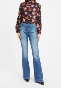 Blouse noire à fleurs avec manches longues, associée à un jean flare bleu clair. Le jean présente une texture délavée et une taille haute.