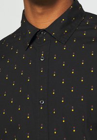 Camisa negra de botones con un patrón repetitivo de pequeños puntos amarillos, rojos y verdes. Hecha de una tela suave con un cuello clásico.