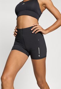 Μαύρα αθλητικά σορτς με ψηλή μέση, κομψό σχεδιασμό και ραφές flatlock, με λευκή λεπτομέρεια λογότυπου στο κάτω δεξί μέρος.