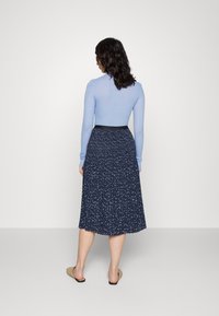 Svetle modré tričko s dlouhým rukávem v kombinaci s námořnickou plisovanou sukní s bílým květinovým vzorem. Hladká tkanina a černý detail na pásku.