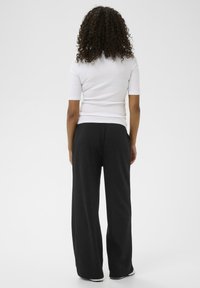 Hvid, tætsiddende kortærmet top parret med løstsiddende sorte bukser. Outfittet har en glat tekstur og et enkelt, minimalistisk design.