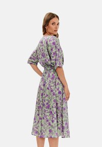 Kvetinové šaty s zeleným pozadím a fialovými kvetmi. Majú krátke, naskladané rukávy, voľný strih a zúžený pás.