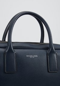 Sac à main en cuir texturé bleu marine avec poignées arrondies et logo argenté « Michael Kors EST. 1981 » centré sous la fermeture éclair.