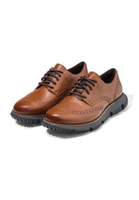 Hnědé kožené boty s designem wingtip, obsahující perforované detaily, černé šnůrky a texturovanou gumovou podrážku.