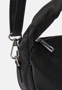 Borsa in tessuto nero con chiusura a zip, dotata di una clip metallica e tracolla. Superficie texturizzata con una finitura liscia e cuciture pulite.