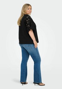 Black top with lace sleeves, paired with blue flared jeans. Material appears soft; the top features a relaxed fit and intricate sleeve detailing.