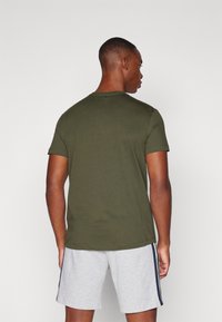 Oliven grøn bomulds t-shirt med korte ærmer og rund hals, parret med grå shorts med sidelister.