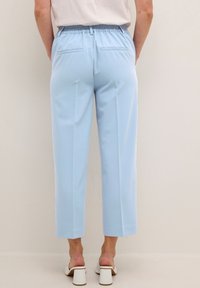 Pantalon bleu clair à coupe décontractée, taille élastique et deux poches arrière. Longueur raccourcie et texture lisse. Associé à des sandales blanches à talons.