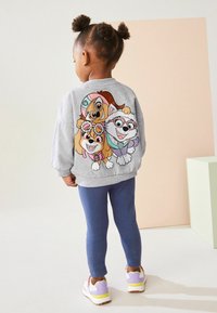Szara bluza z kolorową grafiką trzech rysunkowych psów z tyłu. W połączeniu z niebieskimi legginsami i kolorowymi sneakersami.