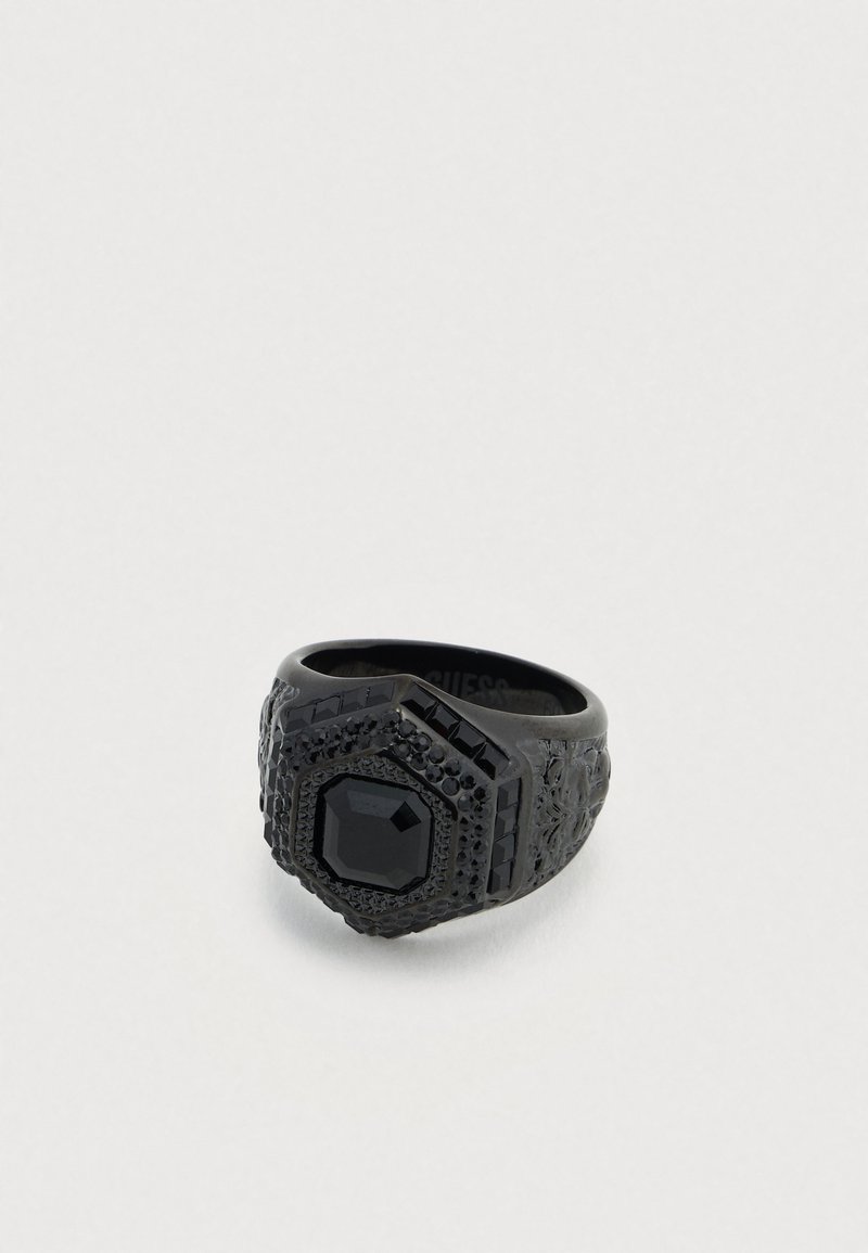 Bague noire au design hexagonal, ornée d'une pierre précieuse noire centrale et de détails texturés le long de l'anneau. Accents délicatement en relief partout.