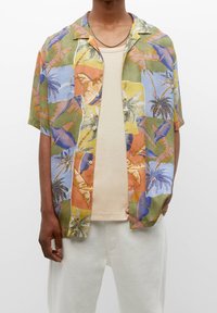 Chemisette multicolore avec un motif tropical de palmiers et d'oiseaux, confectionnée dans un tissu léger. Assortie à un débardeur beige.