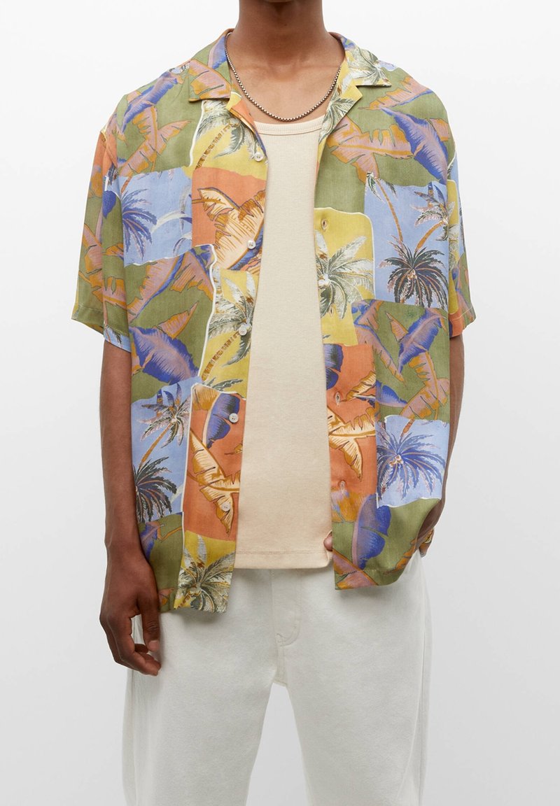 Chemisette multicolore avec un motif tropical de palmiers et d'oiseaux, confectionnée dans un tissu léger. Assortie à un débardeur beige.
