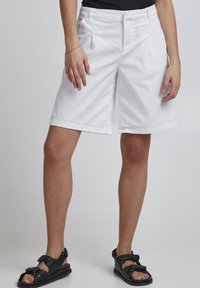 Hvide bomuldsshorts med en afslappet pasform, foran lommer og en foldet kant. Sammen med sorte justerbare sandaler.