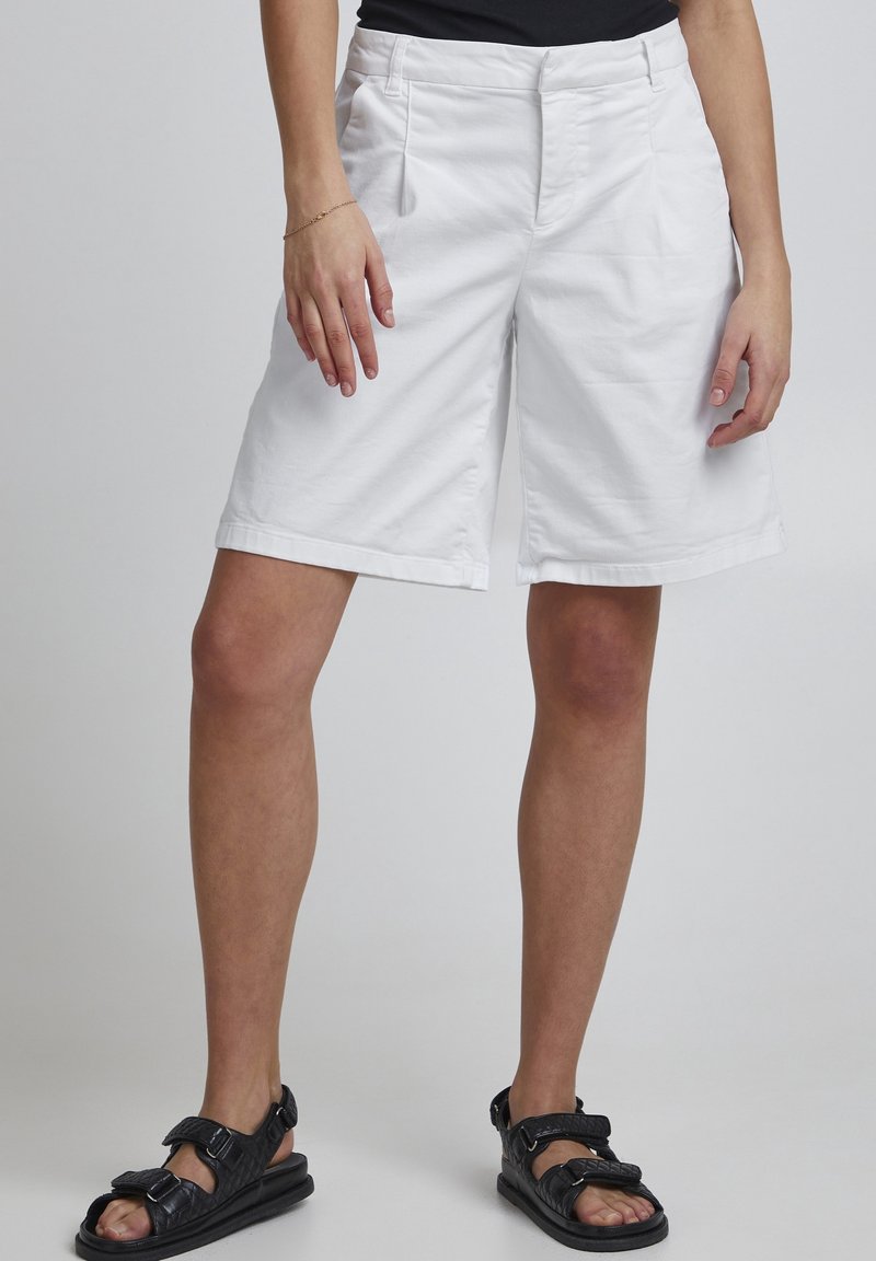 Hvide bomuldsshorts med en afslappet pasform, foran lommer og en foldet kant. Sammen med sorte justerbare sandaler.