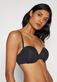 Sostén negro acolchado con tejido suave, tirantes finos ajustables y un diseño sin costuras. Presenta una forma de copa redondeada y un cierre básico de gancho.