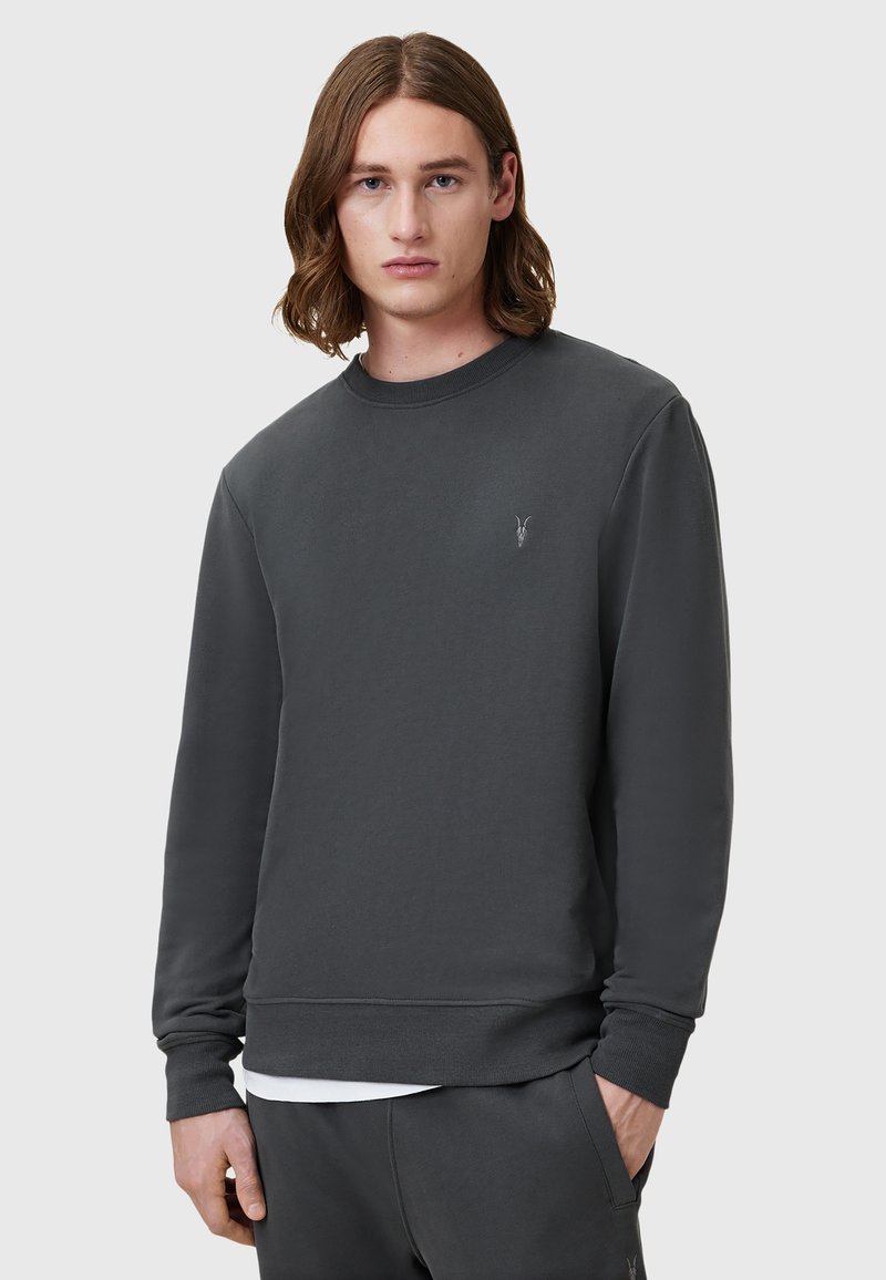 Sudadera gris oscuro hecha de material suave, con cuello redondo, mangas largas y un pequeño logo bordado en el pecho.