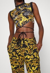 Svart och gul kort topp med blommönster, med utskurna sidor, kombinerad med svarta byxor med ett virvlande gult motiv.