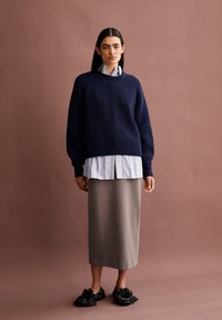 Pull en laine bleu marine, chemise à rayures blanches en dessous, jupe midi grise et chaussures noires avec des franges. Tissu doux et coupe décontractée.