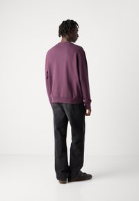Sudadera morada con un corte relajado, puños y cinturilla acanalados, combinada con jeans de mezclilla negros y zapatillas oscuras. Textura lisa.