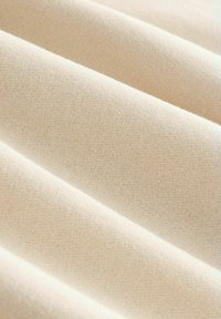 Nahaufnahme eines beigen Stoffes mit sichtbarer feiner Strickstruktur, dargestellt in sanften Falten, die diagonale Linien über den Rahmen ziehen.