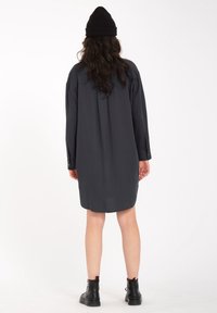 Robe chemise noire à manches longues en tissu léger, avec un fit décontracté, des poignets boutonnés et un ourlet arrondi, associée à des bottines noires à la cheville.