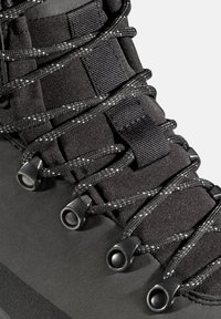 Schwarzer Wanderschuh mit strukturiertem Obermaterial, robustem Schnürsystem und Kunststoffösen. Das Design enthält reflektierende Details in den Schnürsenkeln.